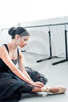 beautiful tender young ballerina sitting and tying pointe