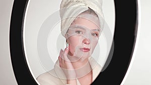 Beautiful tender young girl in a white towel with clean fresh skin posing in front of the camera with a sheet mask on