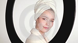 Beautiful tender young girl in a white towel with clean fresh skin posing in front of the camera with a sheet mask on