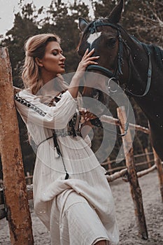 Beautiful and tender young woman wearing the dress is embracing and stroking the horse on the ranch