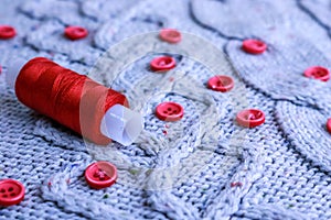 Soft warm natural sweater, fabrics with a knitted pattern of yarn and red small round buttons for sewing and a skein of red thread