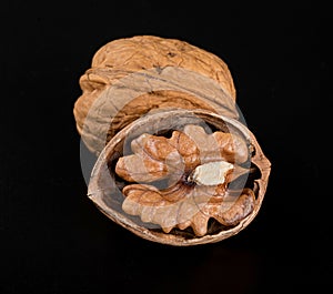A beautiful textured walnut in a shell and a split walnut with half a nut inside on a black background