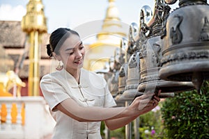 Beautiful Thai-Asian woman in a traditional Thai-Northern dress is ringing temple bells in a temple