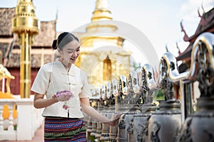 Beautiful Thai-Asian woman in a traditional Thai-Northern dress is ringing temple bells in a temple