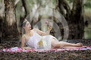 Beautiful Thai asian woman in white dress local tradition costume in the name is Nakee, lying and holding lotus in the botannical photo