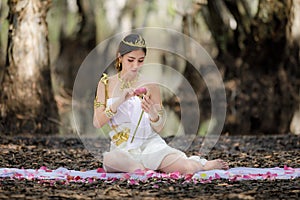 Beautiful Thai asian woman in white dress local tradition costume in the name is Nakee, sitting and holding lotus in the photo