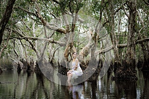 beautiful Thai asian woman in white dress local tradition costume in the name is Nakee, sitting on tree stump in the lake in the