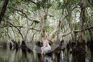 beautiful Thai asian woman in white dress local tradition costume in the name is Nakee, sitting on tree stump in the lake in the