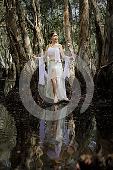 beautiful Thai asian woman in white dress local tradition costume in the name is Nakee, standing on tree in the lake in the