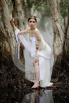 beautiful Thai asian woman in white dress local tradition costume in the name is Nakee, standing on tree in the lake in the