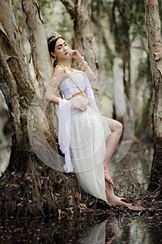beautiful Thai asian woman in white dress local tradition costume in the name is Nakee, standing on tree in the lake in the