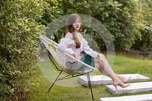 Beautiful Thai woman sittng on metal chair , she sitting outside in the warm sunshine among in green garden