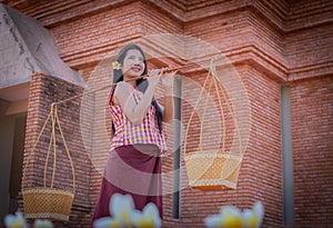 Beautiful thai woman in traditional thai dress is holding a hawker basket in an old temple with a smile