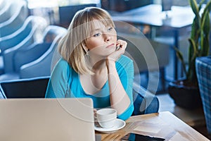 Beautiful thinkful young girl freelancer with blonde bob haircut hair in blue blouse are sitting in cafe and dreaming, having new