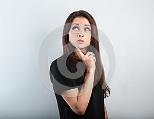 Beautiful thinking angry woman looking up with finger under the face in casual black t-shirt on light blue background with empty