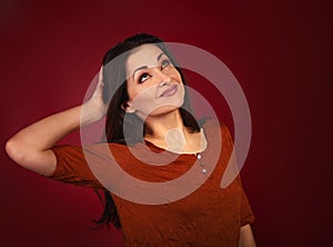 Beautiful thinking smiling woman with hand near the head looking up on dark red background with empty copy space. Closeup portrait