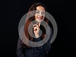Beautiful thinking toothy smiling business woman with finger under the face in blue shirt on black background with empty copy