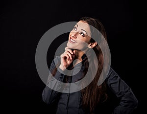 Beautiful thinking toothy smiling business woman with folded arms looking up in blue shirt on black background with empty copy