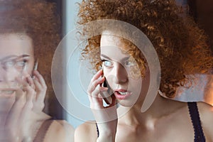 Beautiful thoughtful curly young redhead woman talking on cell phone