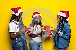 Beautiful three african women holding christmas presents isolated on yellow background