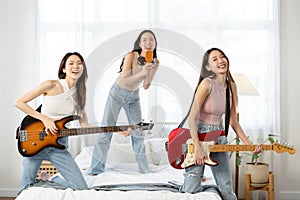 Beautiful three young Asian girls having fun singing and dancing in bedroom. Happy group of Asian friends playing musical