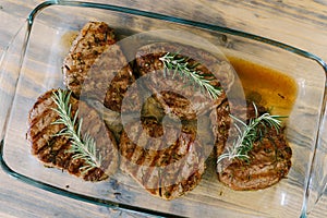 Beautiful toasted steaks in a glass plate on a wooden background, in their own juice and sprigs of rosemary.