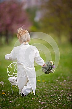 Beautiful toddler boy, dressed in white tuxedo, holding gorgeous flower bouquet for mothers day
