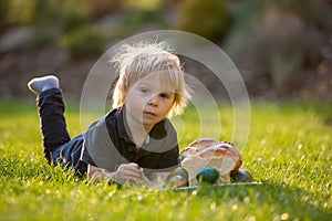 Beautiful toddler boy, eating sweet bread and eggs in garden on sunset, little chicks running around