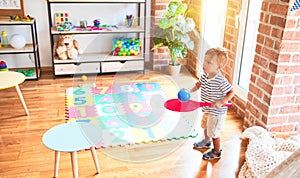 Beautiful toddler boy playing tennis with red racket and ball at kindergarten