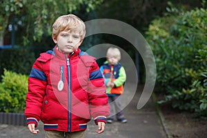 Beautiful toddler boy in red clothes with brother on background.