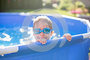 Beautiful toddler child, blond boy, swimming in a pool in backyard