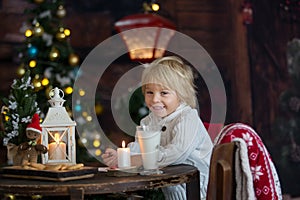 Beautiful toddler child, blond boy, writing letter to Santa Claus and eating cookies at home, cozy atmosphere