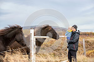 Beautiful toddler child with dad, fondle horses in the nature, early in the morning on a windy autumn day photo