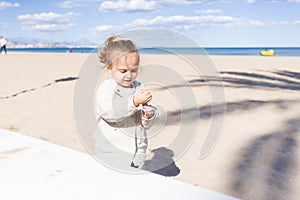 Beautiful toddler child girl wearing jacket playing with the sand on the beach