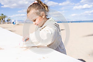 Beautiful toddler child girl wearing jacket playing with the sand on the beach