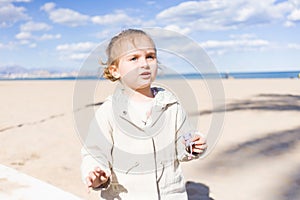 Beautiful toddler child girl wearing jacket playing with the sand on the beach