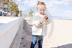 Beautiful toddler child girl wearing jacket playing with the sand on the beach