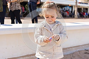 Beautiful toddler child girl wearing jacket playing with the sand on the beach