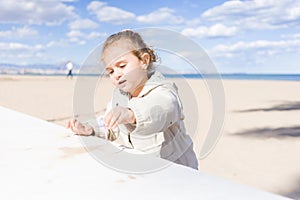 Beautiful toddler child girl wearing jacket playing with the sand on the beach