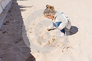 Beautiful toddler child girl wearing jacket playing with the sand on the beach