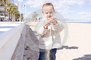 Beautiful toddler child girl wearing jacket playing with the sand on the beach