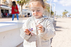 Beautiful toddler child girl wearing jacket playing with the sand on the beach