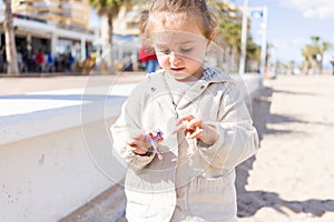 Beautiful toddler child girl wearing jacket playing with the sand on the beach