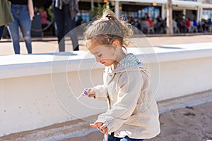 Beautiful toddler child girl wearing jacket playing with the sand on the beach