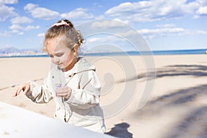 Beautiful toddler child girl wearing jacket playing with the sand on the beach