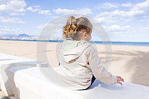 Beautiful toddler child girl wearing jacket sitting on the bench in the promenade