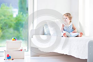 Beautiful toddler girl with curly hair reading book