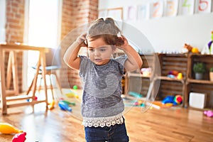 Beautiful toddler standing with hands raised smiling around lots of toys at kindergarten