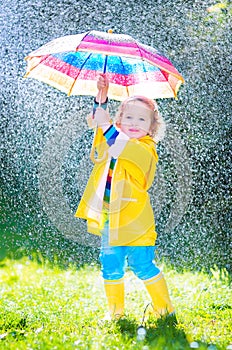 Beautiful toddler with umbrella playing in the rain