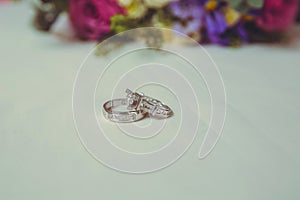 Beautiful toned picture with Engagement rings lie on a wooden surface against the background of a bouquet of flowers . wedding